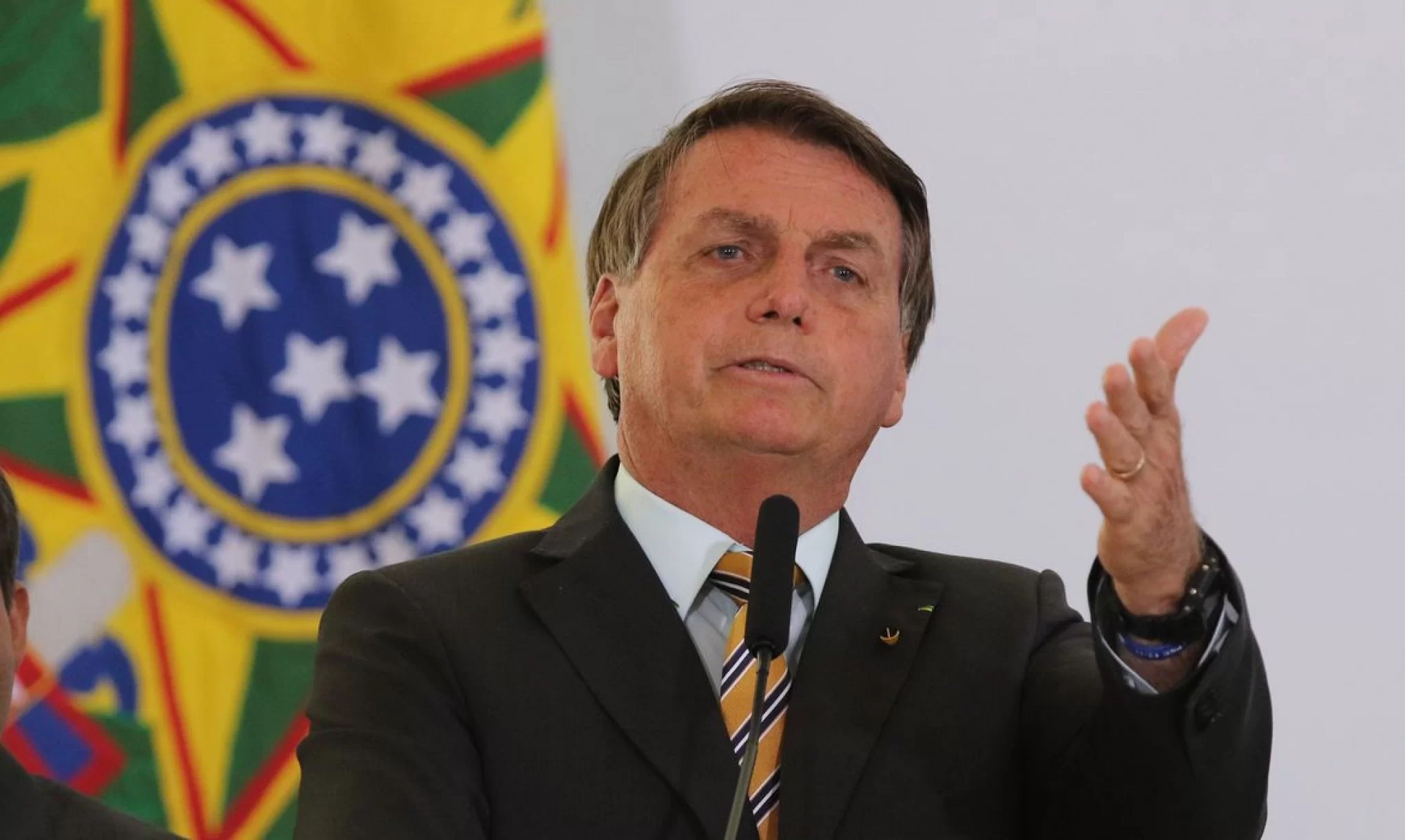 Jair Bolsonaro falando com mão estendida e expressão séria
