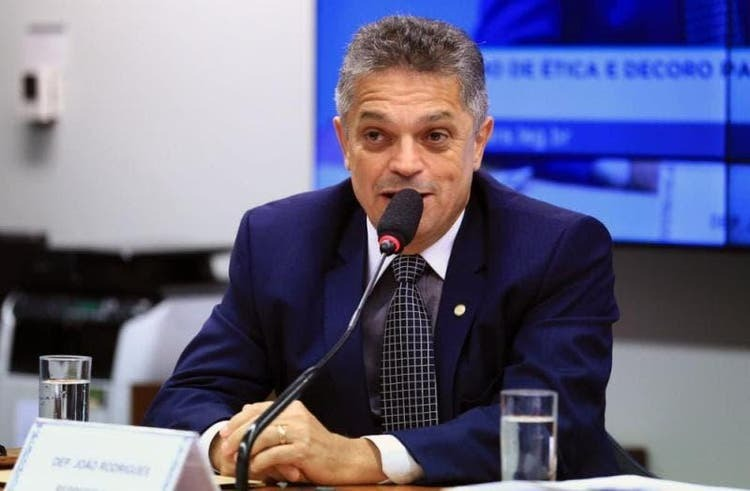 João Rodrigues vestindo roupa social, falando e gesticulando