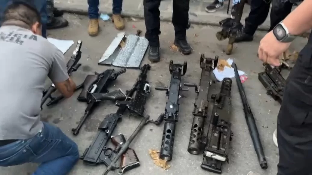 Imagem de armas no chão com pessoas em volta