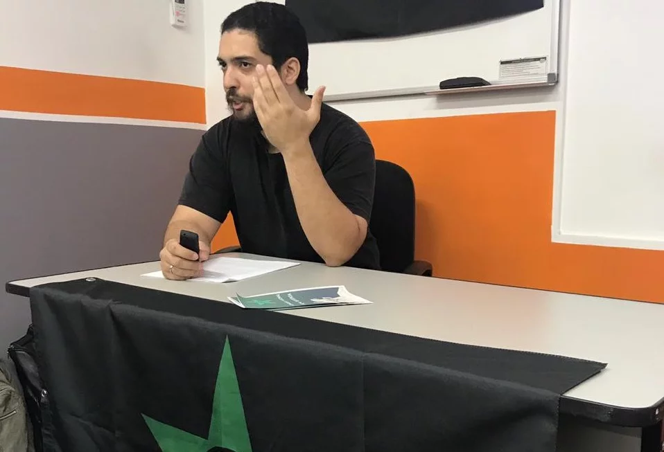 Raphael Machado de roupa preta, falando e gesticulando