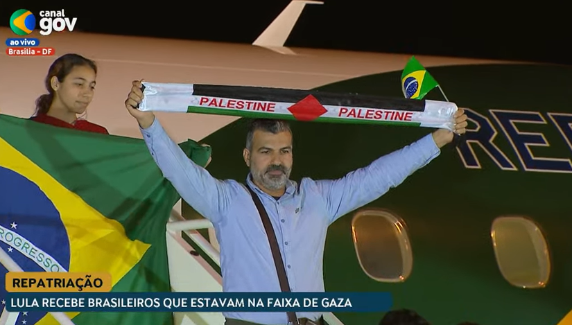 Repatriados descendo do avião com bandeira do Brasil e uma faixa da Palestina
