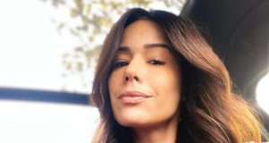 Adriane Garcia de roupa rosa e cabelo solto, dentro de carro, sem sorrir