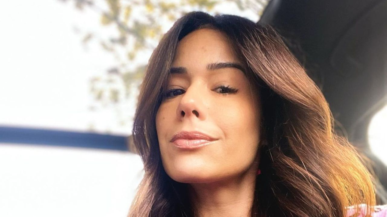 Adriane Garcia de roupa rosa e cabelo solto, dentro de carro, sem sorrir