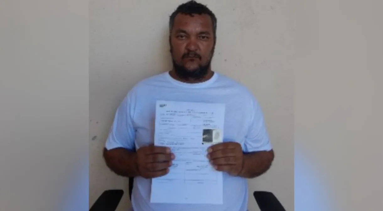 Cleriston Pereira da Cunha posando para foto de roupa branca, segurando papel, com expressão séria
