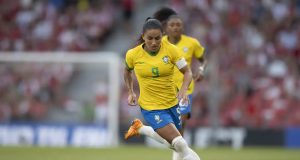 Debinha correndo em campo com uniforme da seleção brasileira