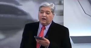 Datena no cenário do Brasil Urgente, segurando celular, com expressão de decepção