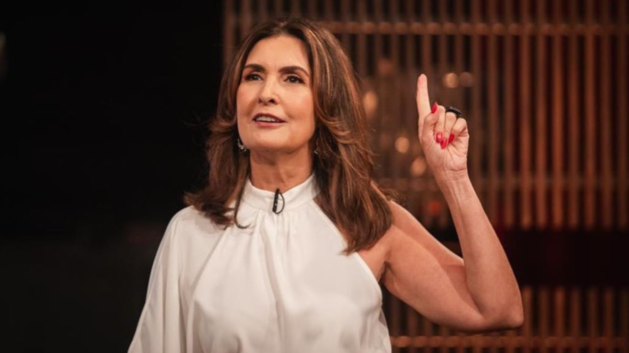 Fátima Bernardes de roupa branca e cabelo solto, apontando pra cima