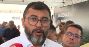 Wilson Lima falando em microfones, usando óculos e roupa branca, olhando pra câmera