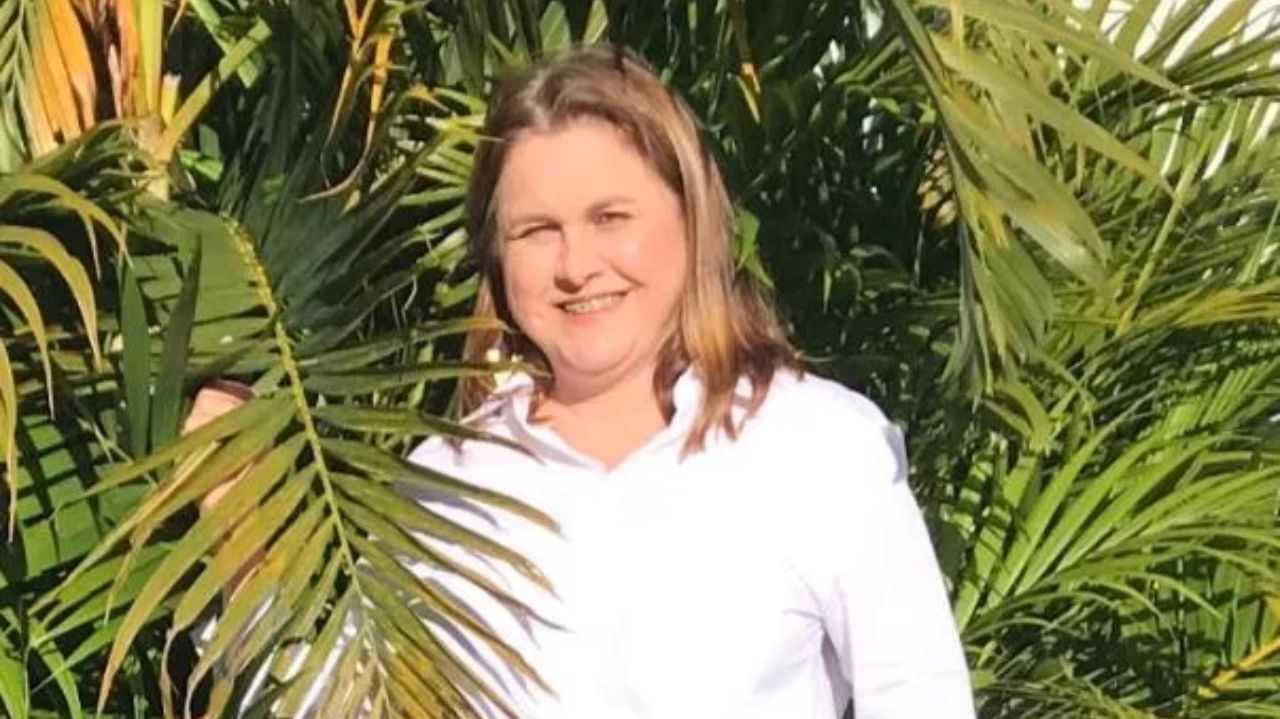Kismara Brustolin sorrindo, de roupa branca, perto de plantas