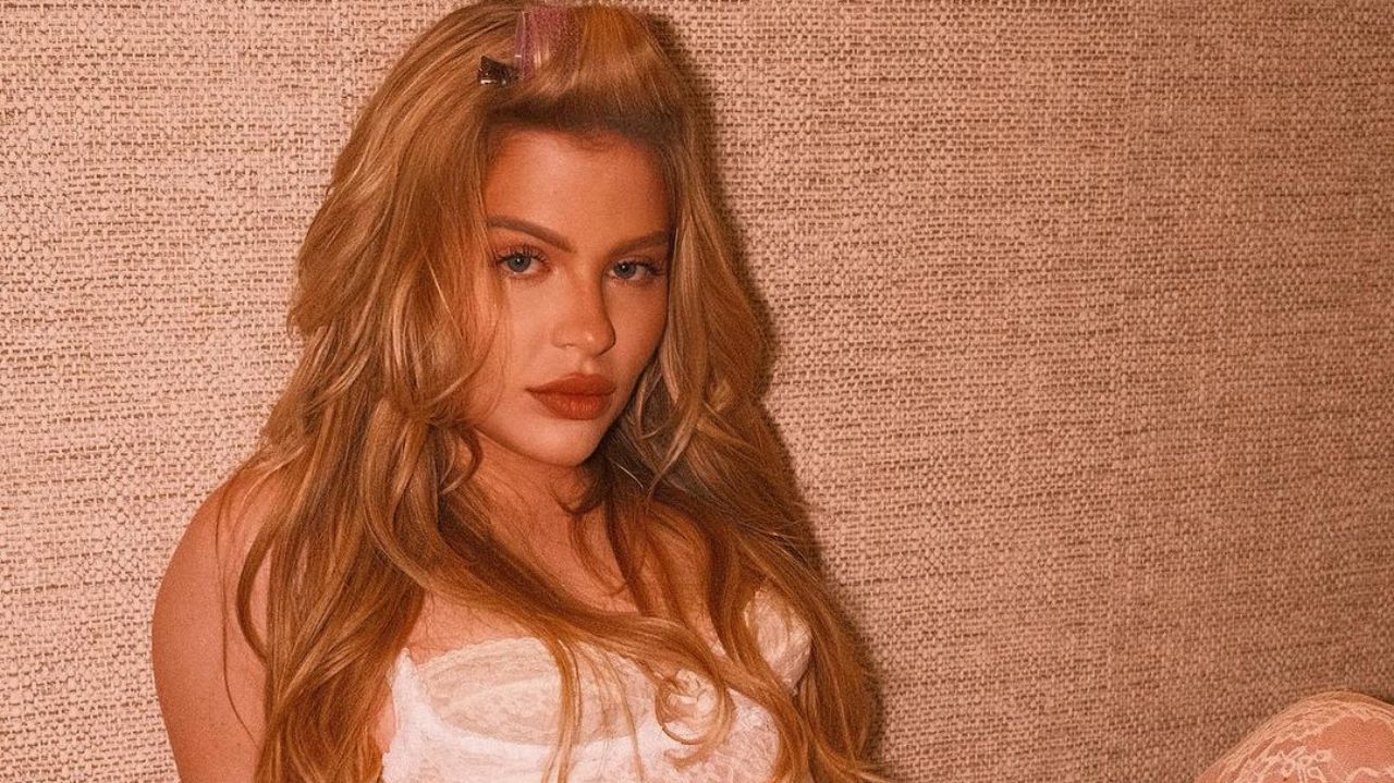 Luísa Sonza de roupa branca e cabelo solto, fazendo carão, encostada em parede