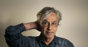 Caetano Veloso com mão na nuca e camisa jeans, sem sorrir