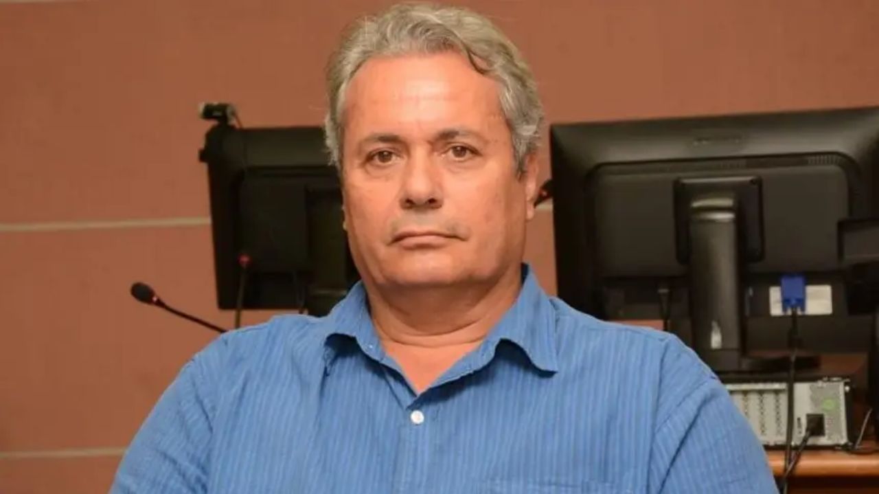 Naçoitan Leite olhando pra câmera com expressão séria, perto de computador, de roupa azul