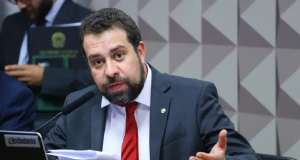 Guilherme Boulos falando em microfone, segurando papel e gesticulando