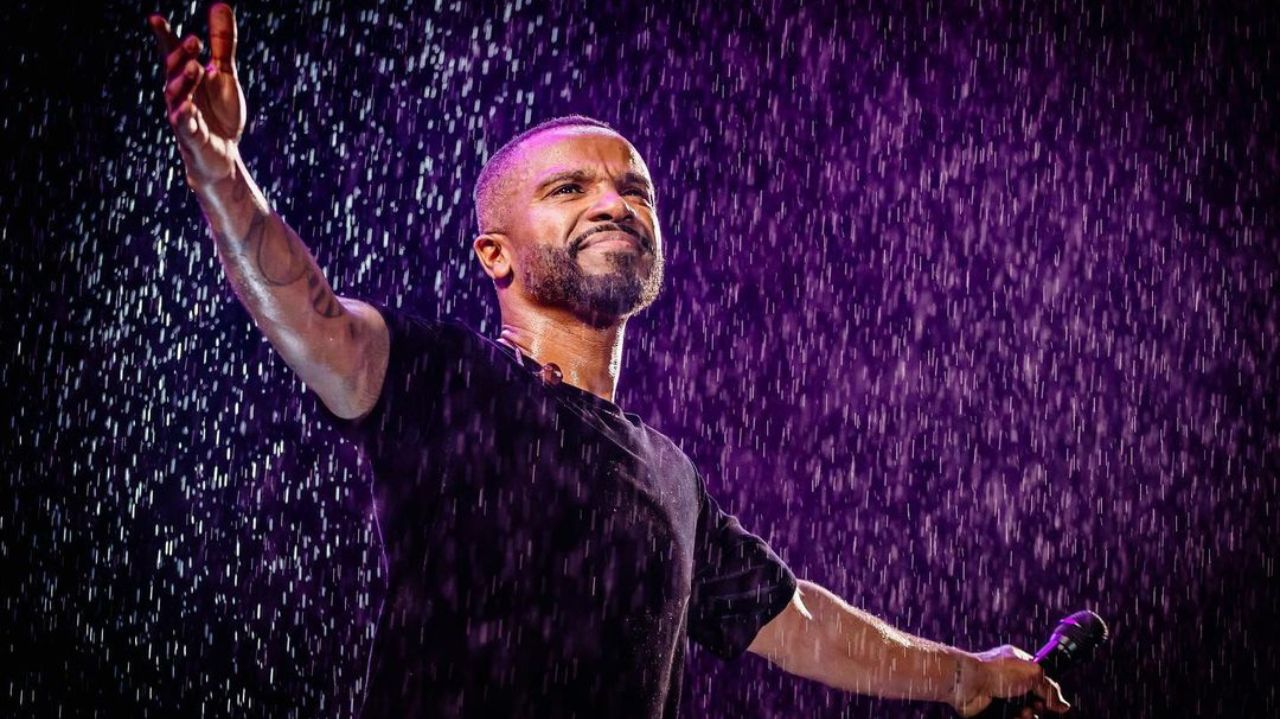 Alexandre Pires de roupa preta, com braços abertos, na chuva