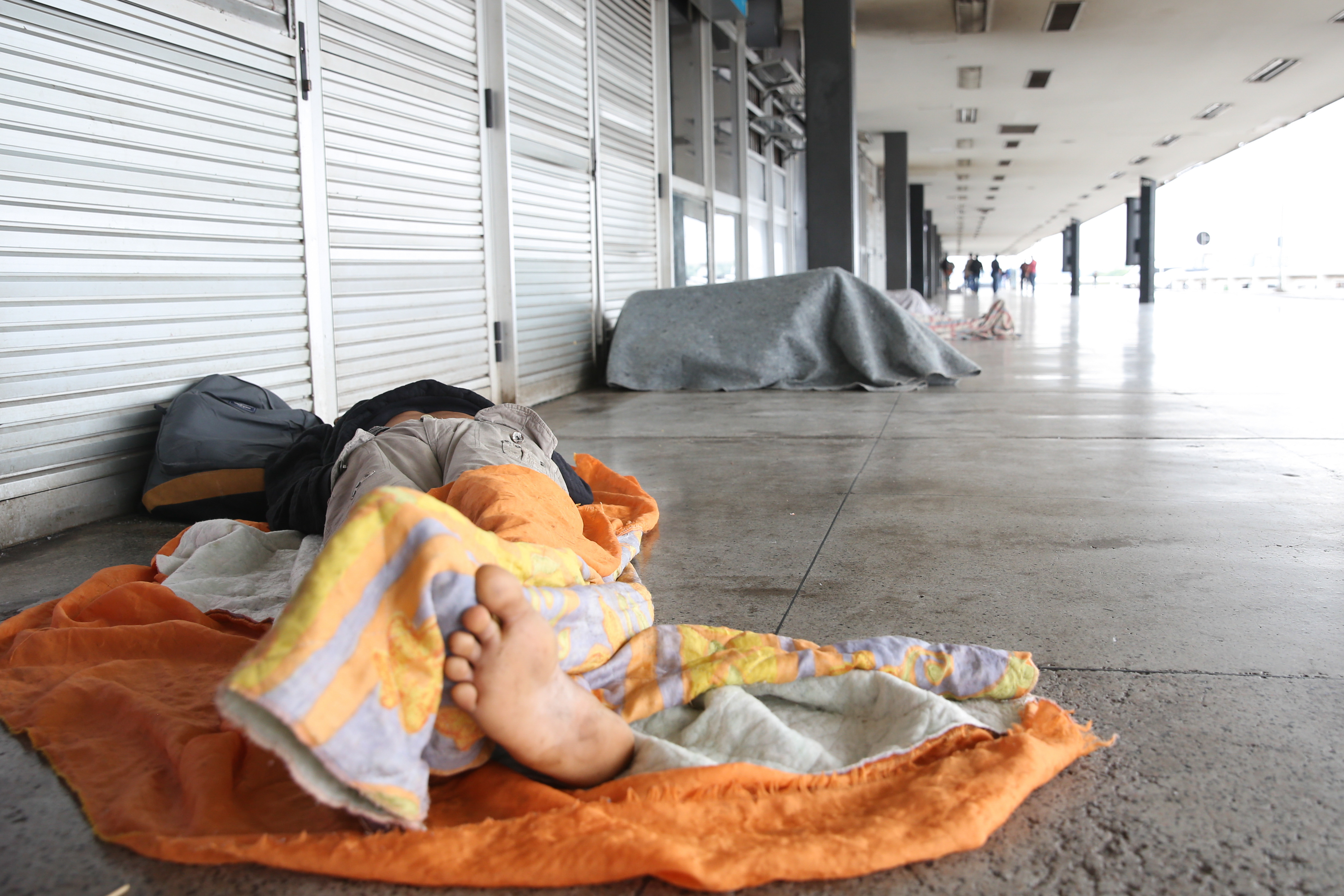 Pessoa em situação de rua dormindo coberta, pé em destaque