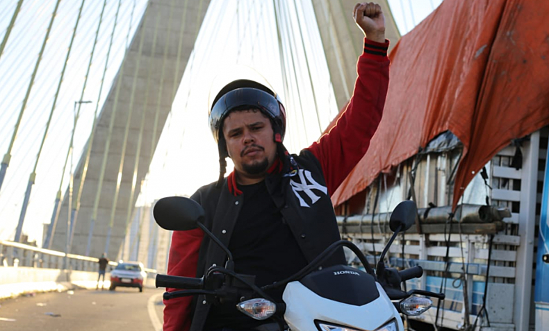 Paulo Galo em cima de moto, com braço levantado em ponte