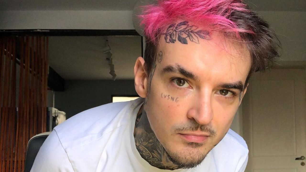 PC Siqueira de cabelo rosa e camisa branca, com expressão séria