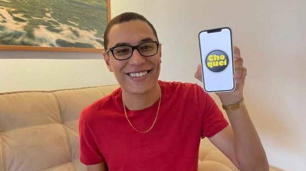 Raphael Sousa de camisa vermelha segurando celular com o logo da Choquei