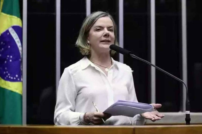 Gleisi Hoffmann de roupa branca, falando em microfone e segurando papel