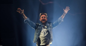 David Guetta em show, com jaqueta jeans e os braços abertos