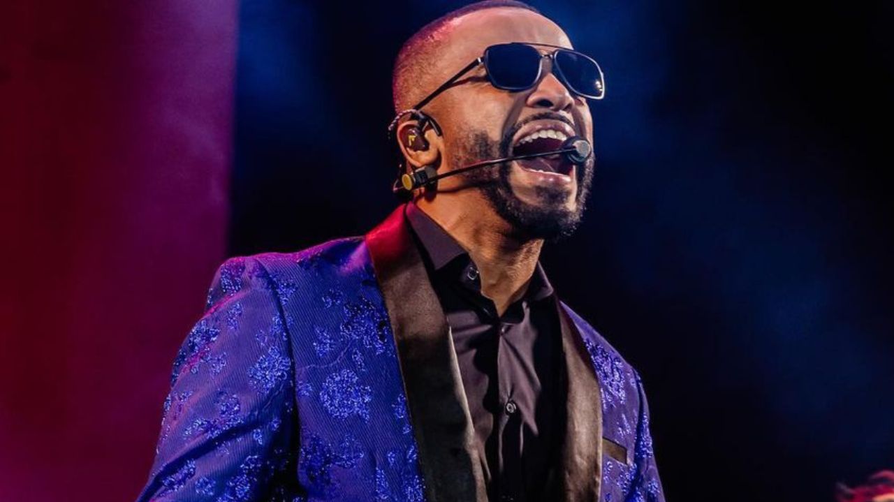 Alexandre Pires de paletó azul e óculos escuros, cantando
