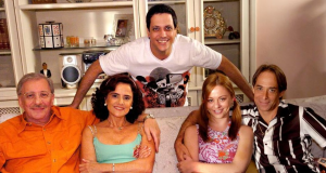 Elenco de A Grande Família posando e sorrindo para foto em cenário da série