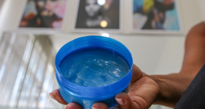 Mão mostrando pote com pomada de cabelo azul para a câmera