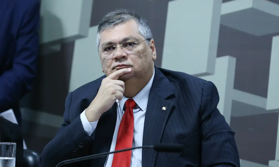 Flávio Dino com expressão pensativa e mão no queixo