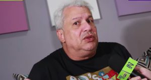 Sikêra Jr. de camiseta preta, falando em microfone, com expressão confusa