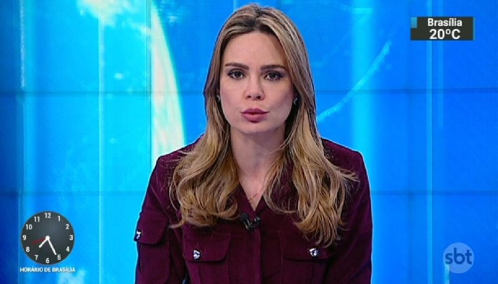 Rachel Sheherazade de roupa cor de vinho, falando para a câmera em estúdio de telejornal, de cabelo solto