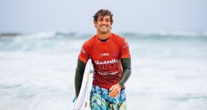 Chumbinho saindo do mar com prancha, sorridente