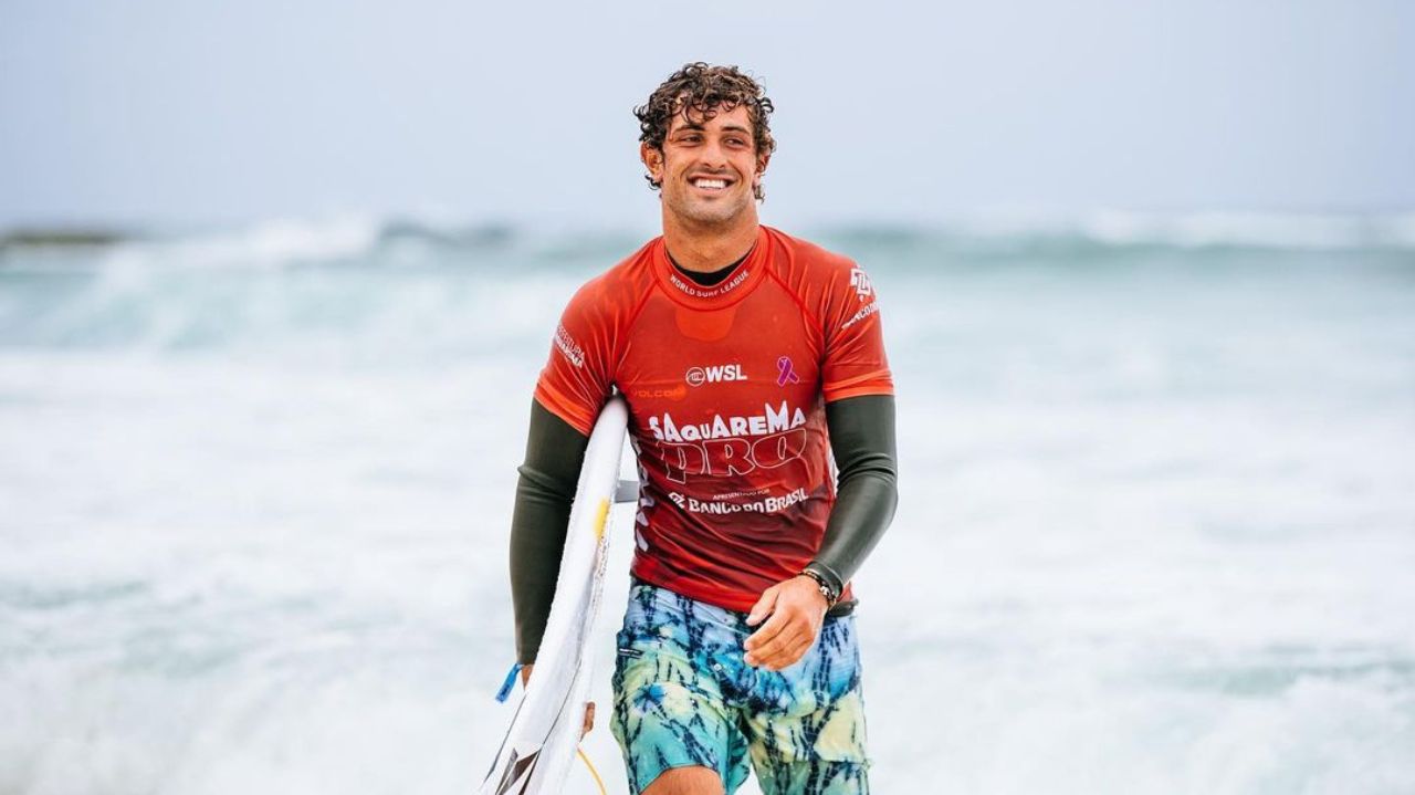 Chumbinho saindo do mar com prancha, sorridente