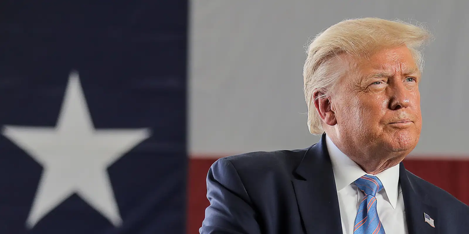 Donald Trump olhando para o lado perto de bandeira dos EUA