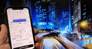 Mão segurando celular com tela do Uber aberta e cidade ao fundo