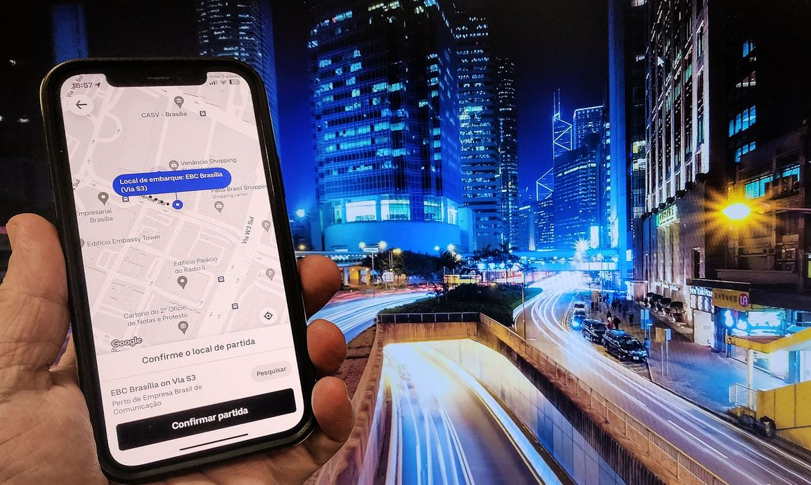 Mão segurando celular com tela do Uber aberta e cidade ao fundo
