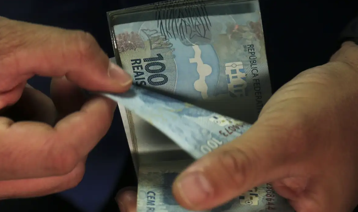 Mãos contando notas de cem reais
