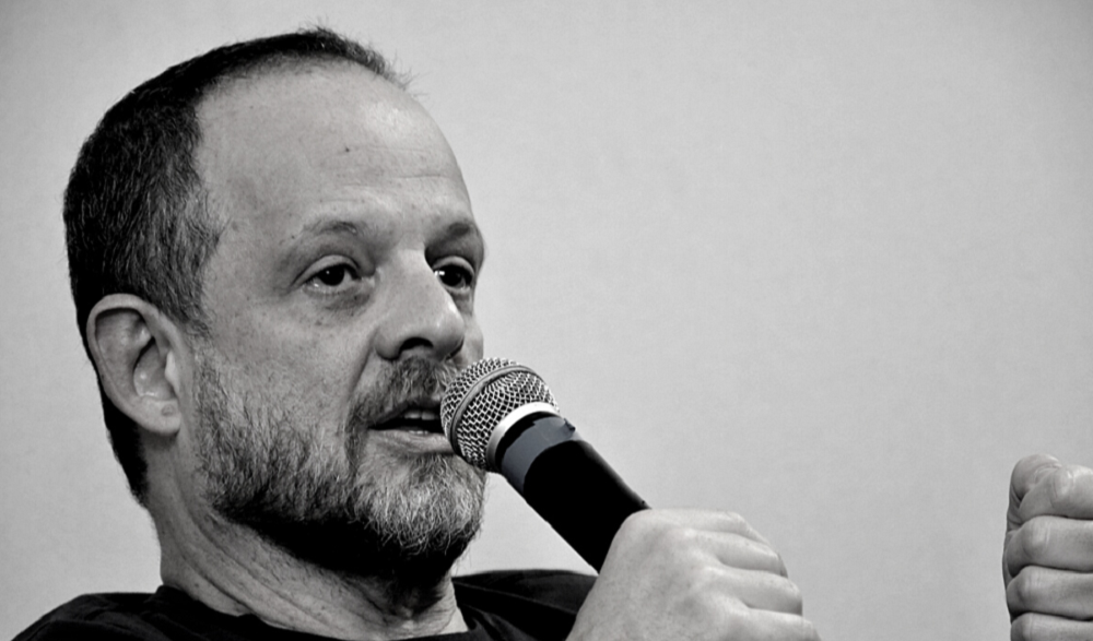 Breno Altman de perfil, falando em microfone, em foto em preto e branco