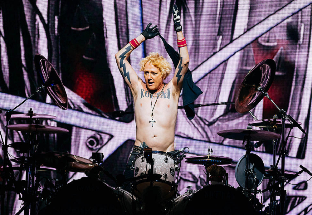 James Kottak com os braços para o alto atrás de bateria