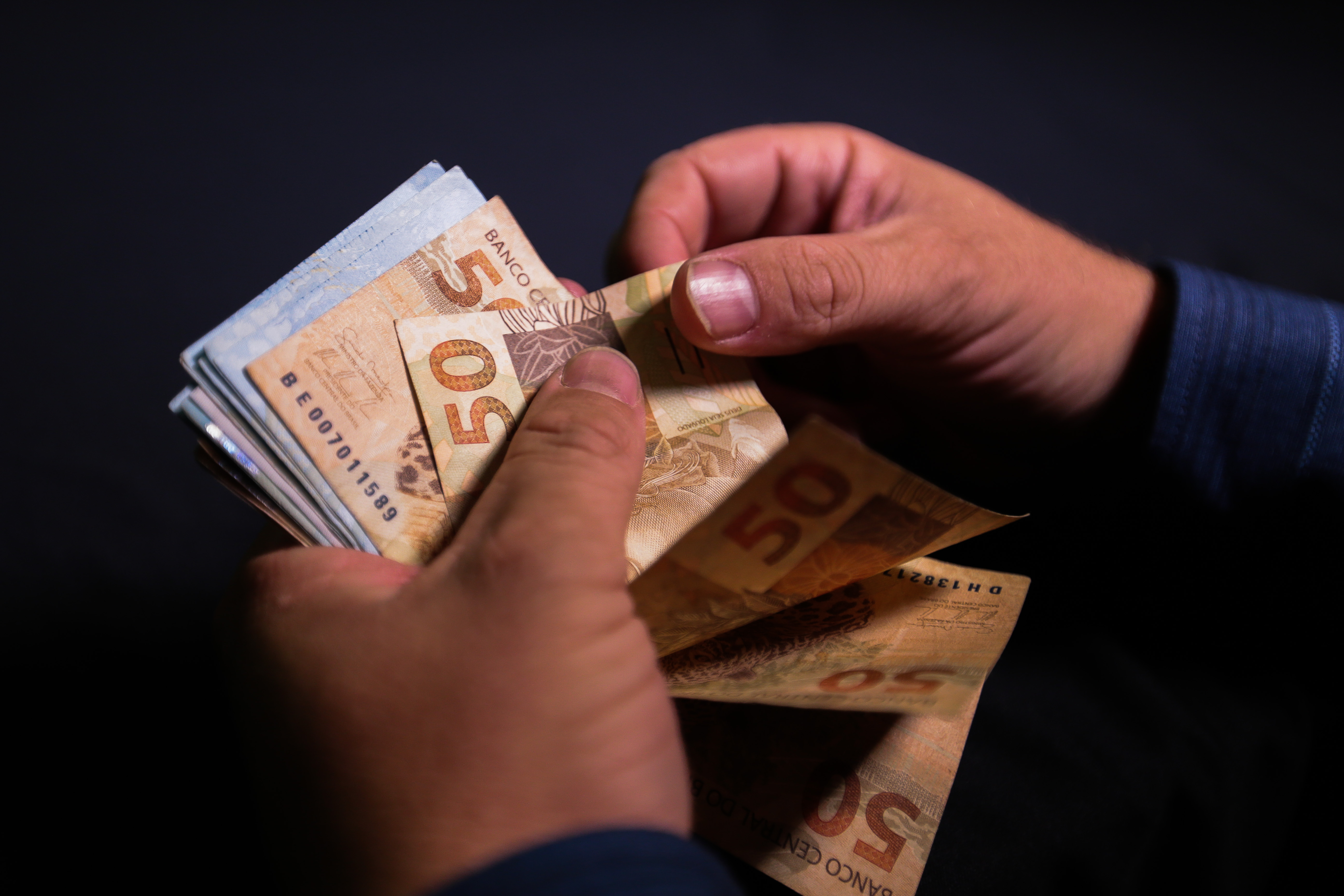 Mãos contando cédulas de reais