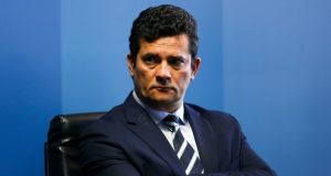 Sergio Moro com os braços cruzados e expressão séria, olhando para o lado