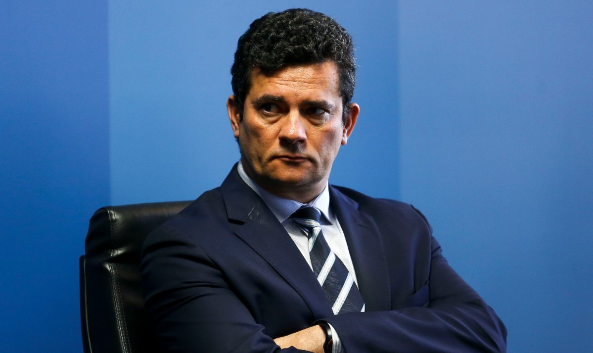 Sergio Moro com os braços cruzados e expressão séria, olhando para o lado