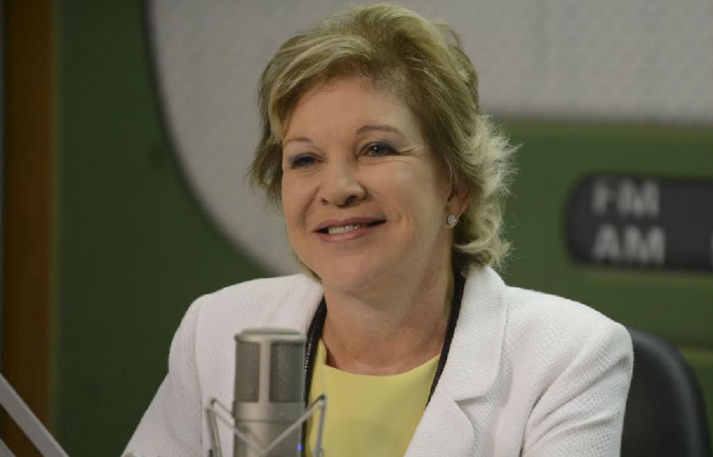 Marta Suplicy de roupa branca e amarela, sorrindo perto de microfone