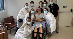 Mingau em cadeira de rodas, rodeado por médicos, olhando para a câmera