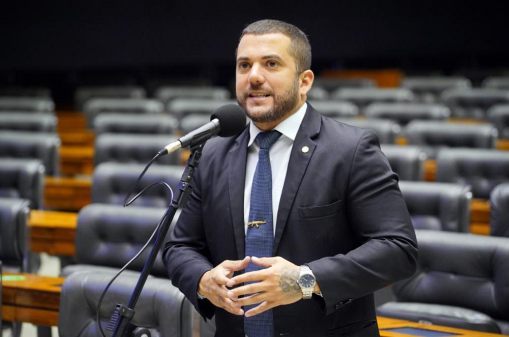 Carlos Jordy de terno e gravata, falando em microfone