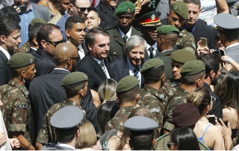 Jair Bolsonaro cercado por militares, com expressão séria