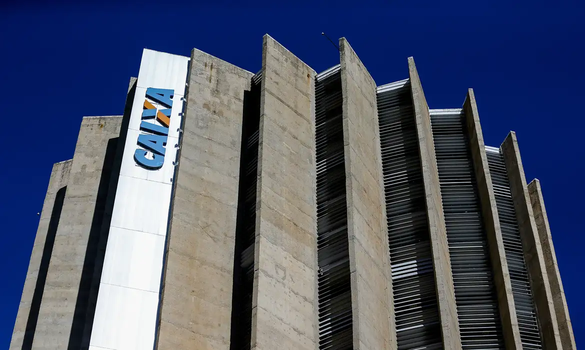 Topo de prédio da Caixa Econômica Federal com céu azul no fundo