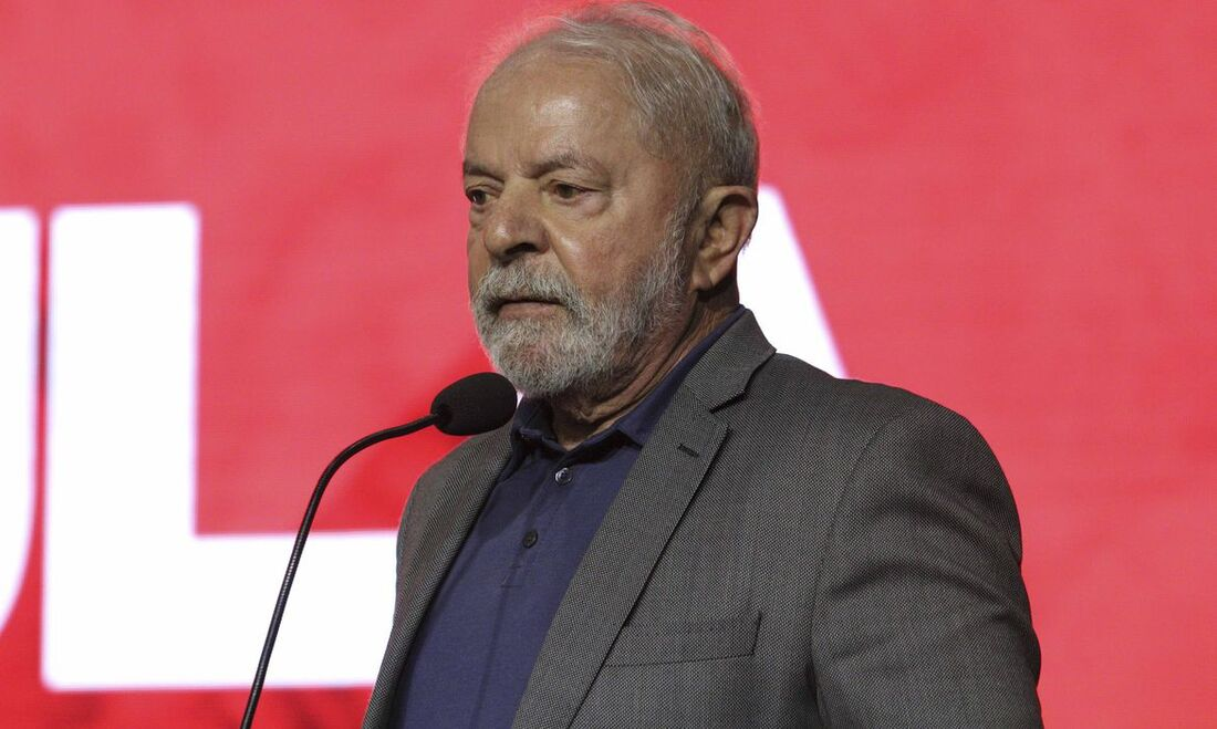 Lula com expressão séria, olhando para o lado, em fundo vermelho