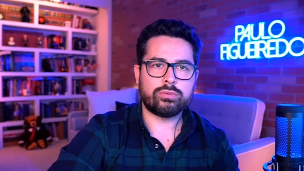 Paulo Figueiredo com expressão séria, em estúdio, de óculos