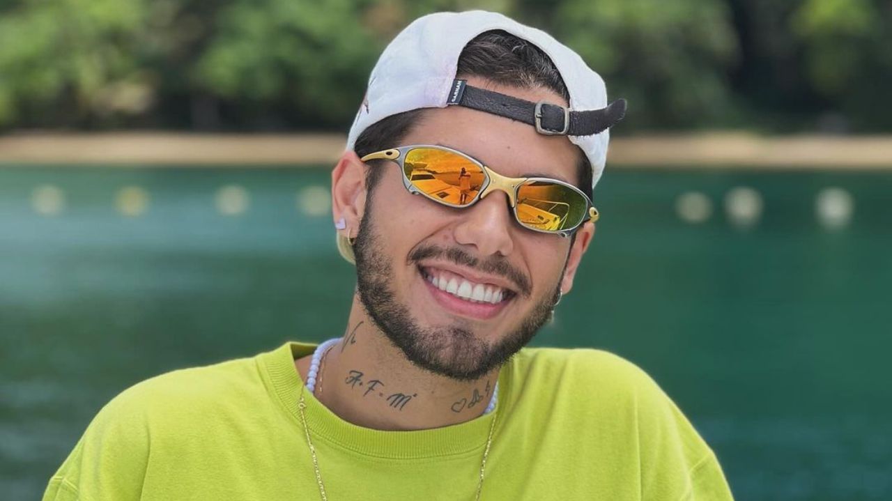Zé Felipe sorrindo para foto de camiseta verde, boné branco para trás e óculos espelhado