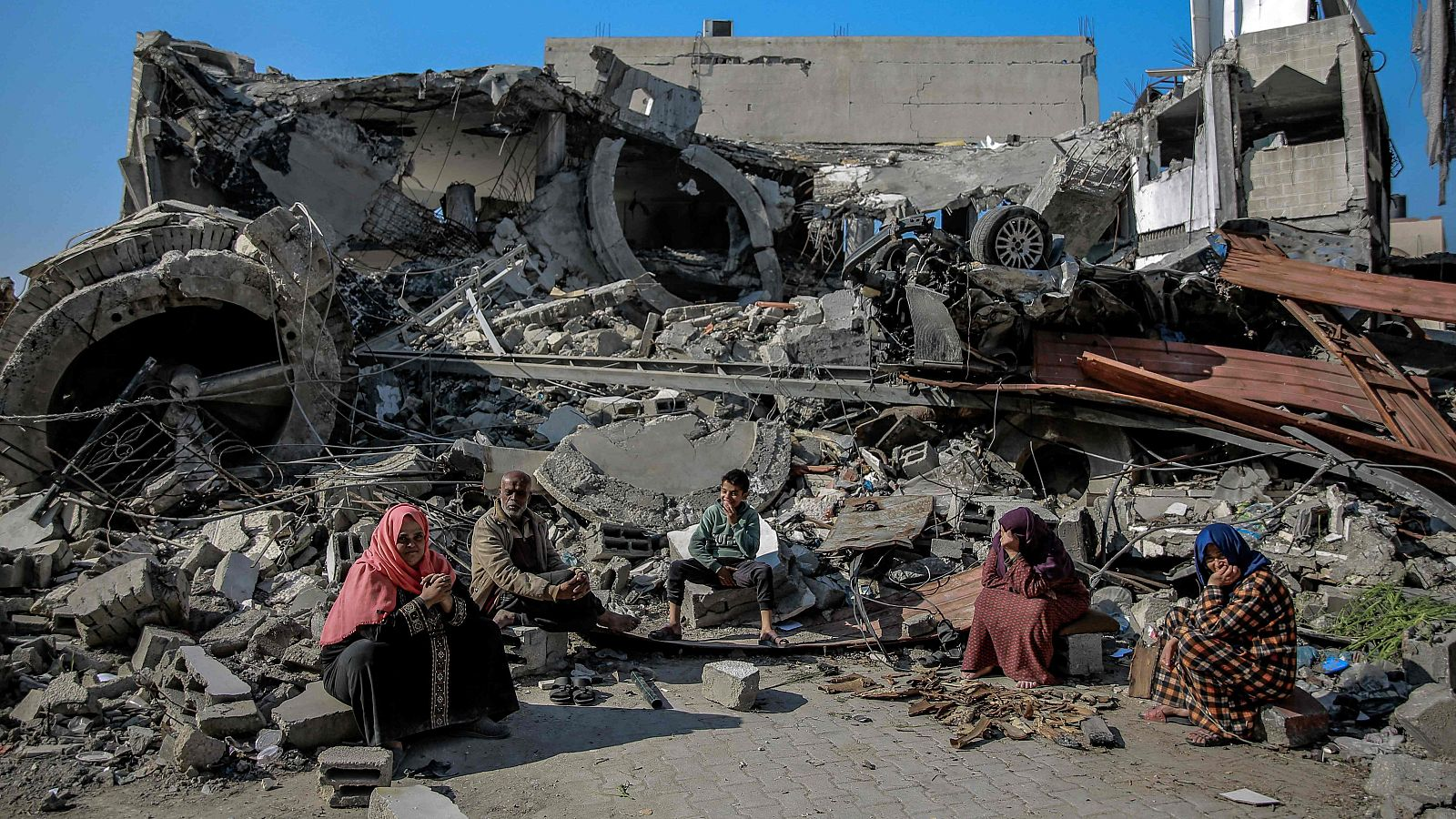 Palestinos sentados em meio a destroços em Gaza